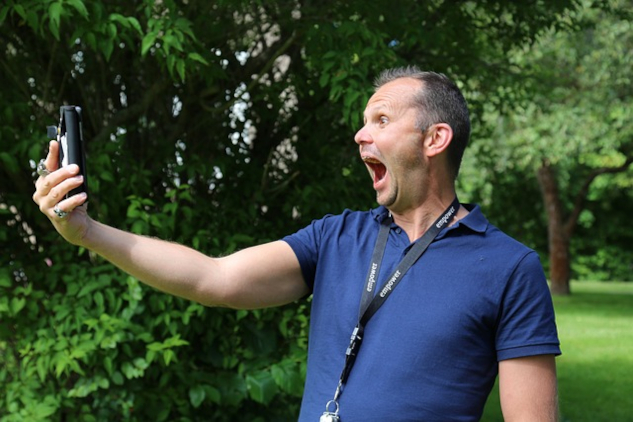 a man shouting into his cell phone which he is holding a arm's length